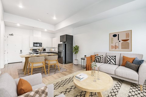 A modern living room with a grey sofa, wooden coffee table, and a kitchen area in the background.