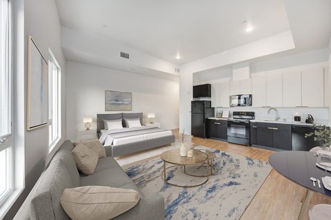 A modern living room with a grey couch and a bed in the background.
