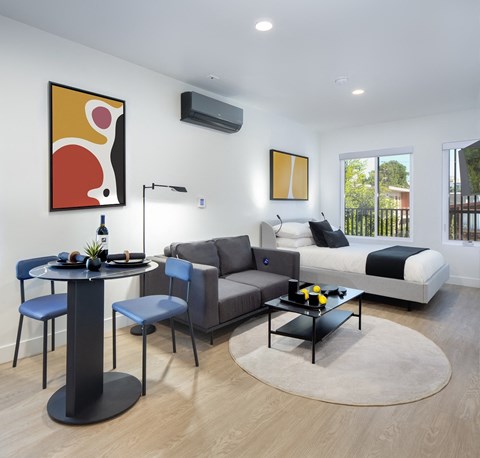 A modern living room with a grey sofa, a black coffee table, and a round table with blue chairs.
