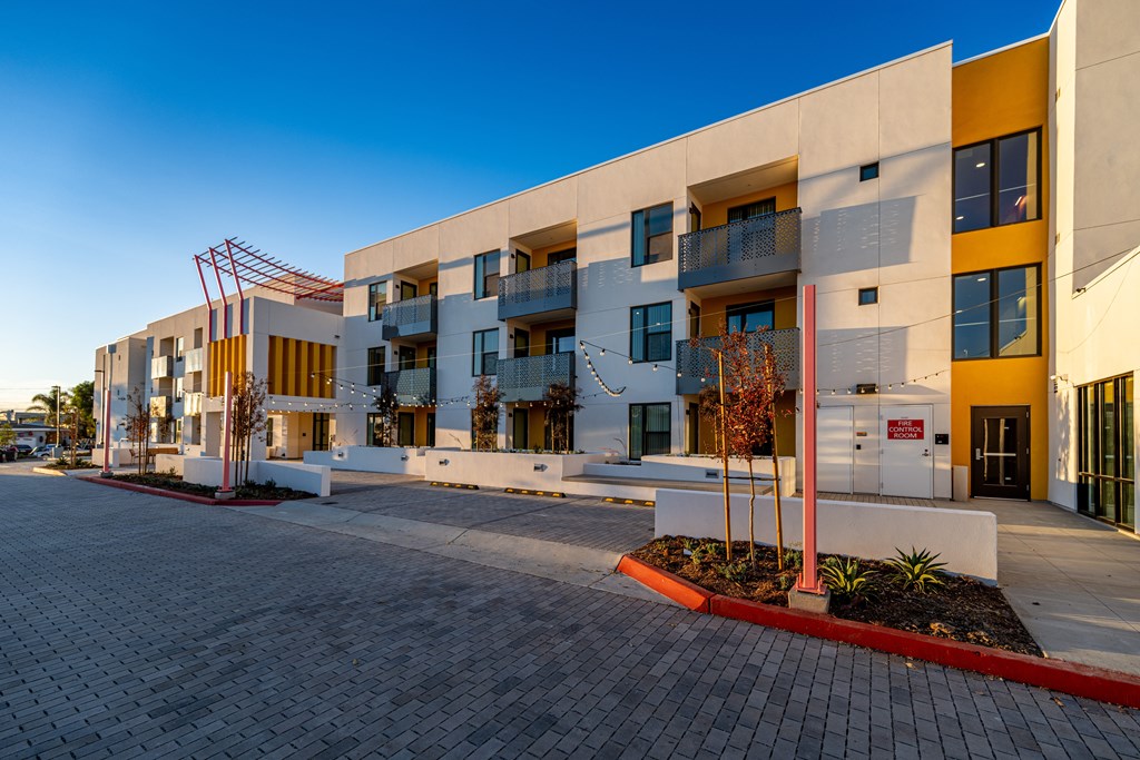 A modern building with a white and yellow facade and a red brick walkway in front.