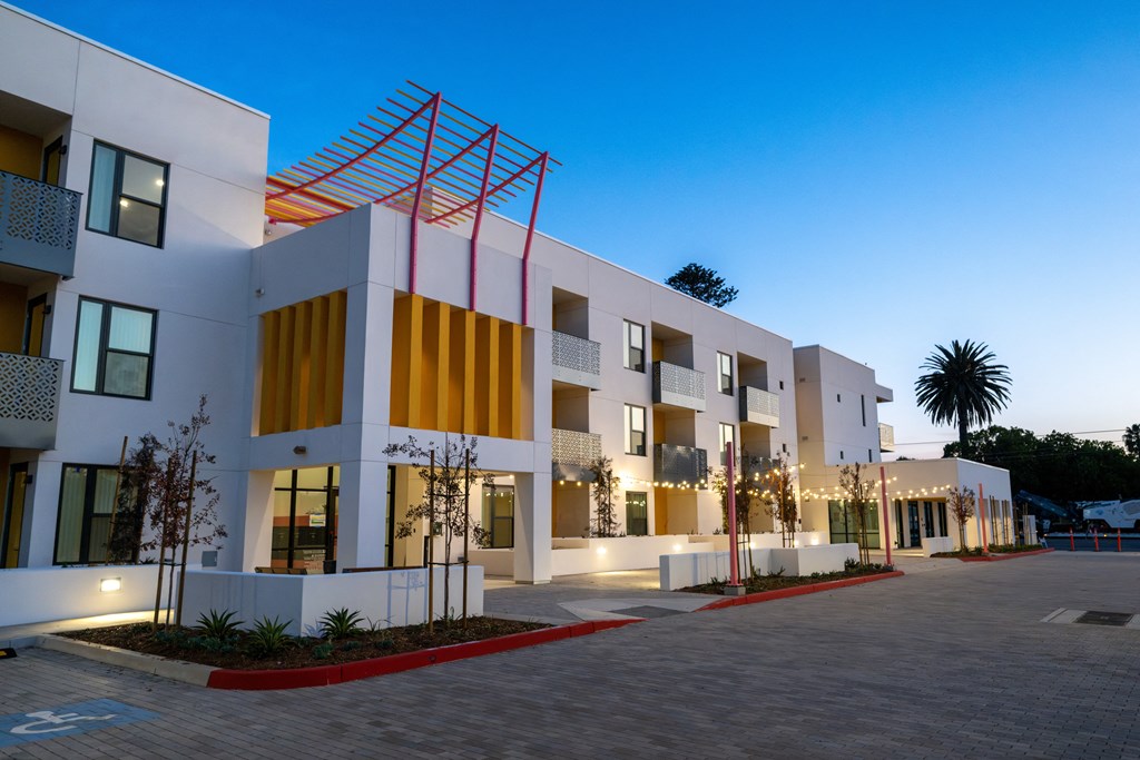 A modern building with a red and yellow accent wall is illuminated at dusk.