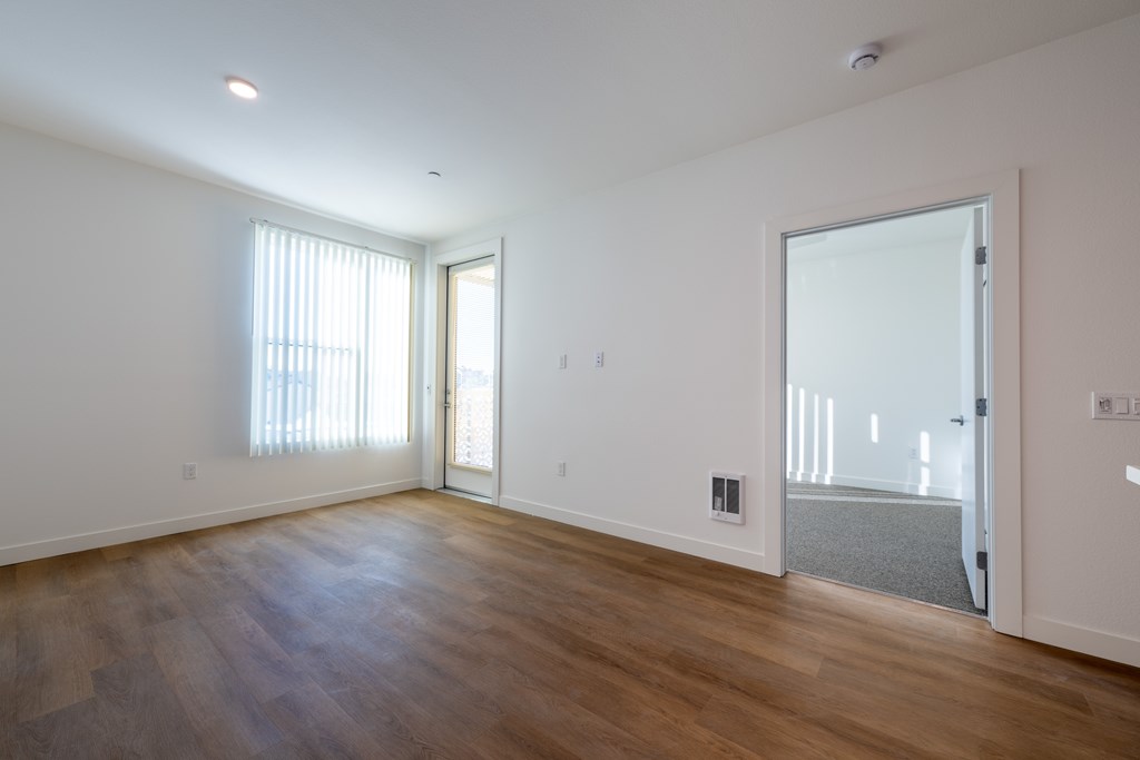 A room with wooden floors and a large window with blinds.