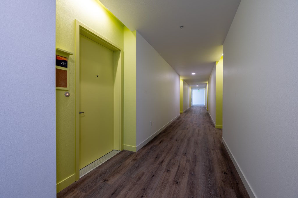 A long hallway with a yellow door on the left and a white door on the right.