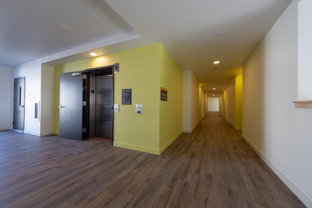 A long hallway with a yellow wall and a black door.