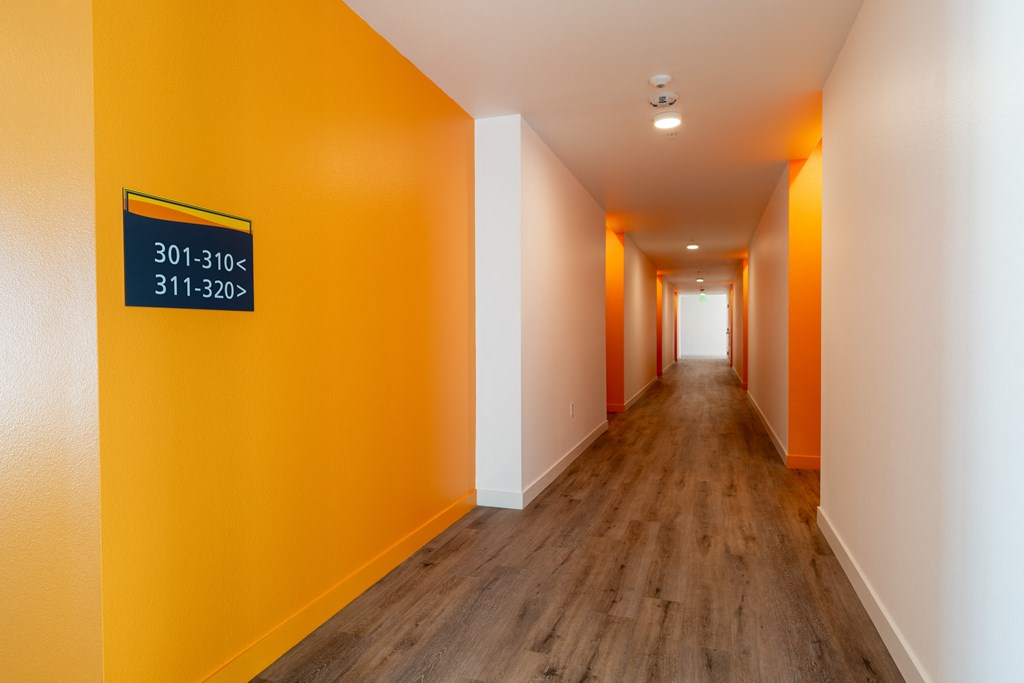 A long hallway with orange walls and wood floors.