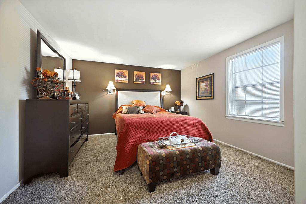 Bedroom in a 2-bedroom Ashton Pointe apartment, featuring carpeted flooring and natural light streaming through a window.