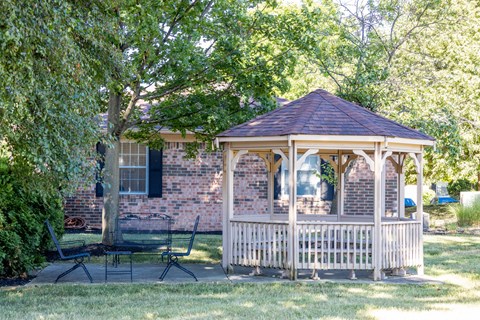 A gazebo is situated in a grassy area in front of a brick house.