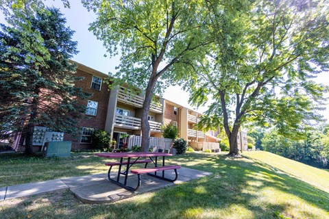 A picnic table is in front of a building and a tree.