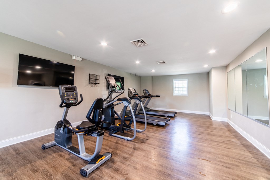 Fitness center at Ashton Brook Apartments features cardio equipment, televisions, and a large mirror