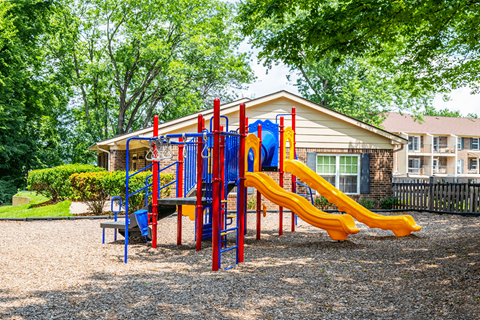 A playground with a red and yellow slide in front of a building.