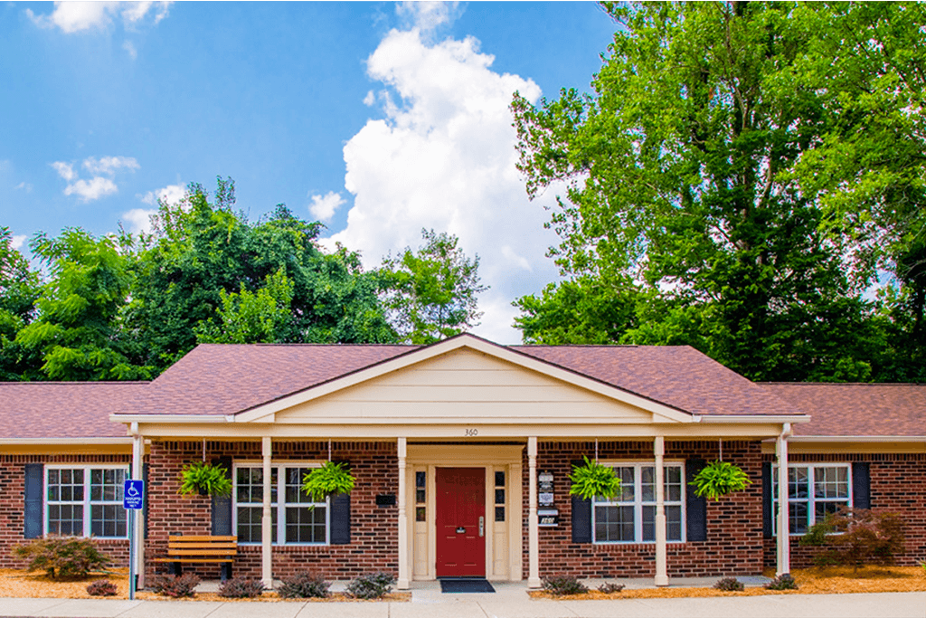 A small building with a red door and windows surrounded by greenery.