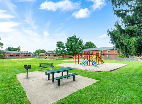 A playground with a green picnic table and a red swing set.