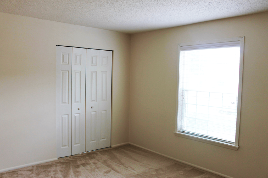 Carpeted bedroom with a window and closet at Cambridge Square Apartments Fort Wayne.