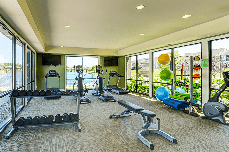 Fitness center at Somerset Lakes Apartments, featuring dumbbells, a bench press, and cardio workout equipment.