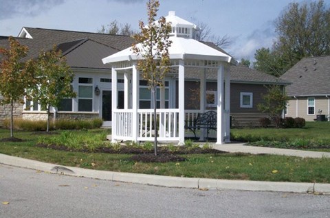 A white gazebo with a tree in front of a grey house.