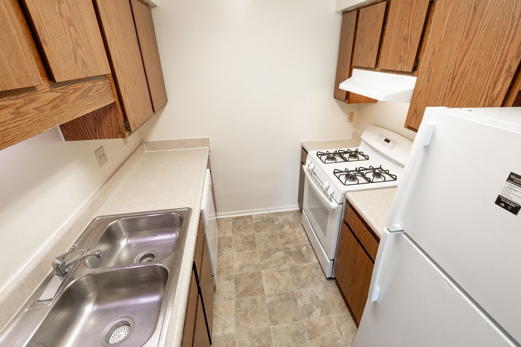 2 bedroom apartment kitchen with white appliances and brown cabinets at Woodbridge Apartments