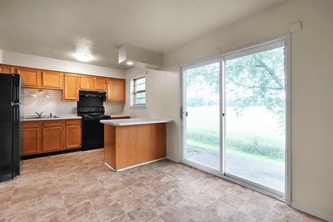A kitchen with a black refrigerator, wooden cabinets, and a black stove top oven.
