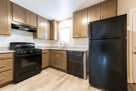 A black refrigerator stands in a kitchen with wooden cabinets and a black stove.