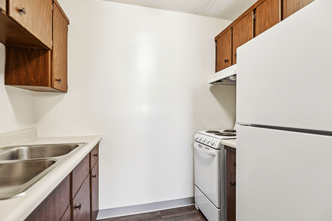A kitchen with a white refrigerator, a stainless steel sink, and wooden cabinets.