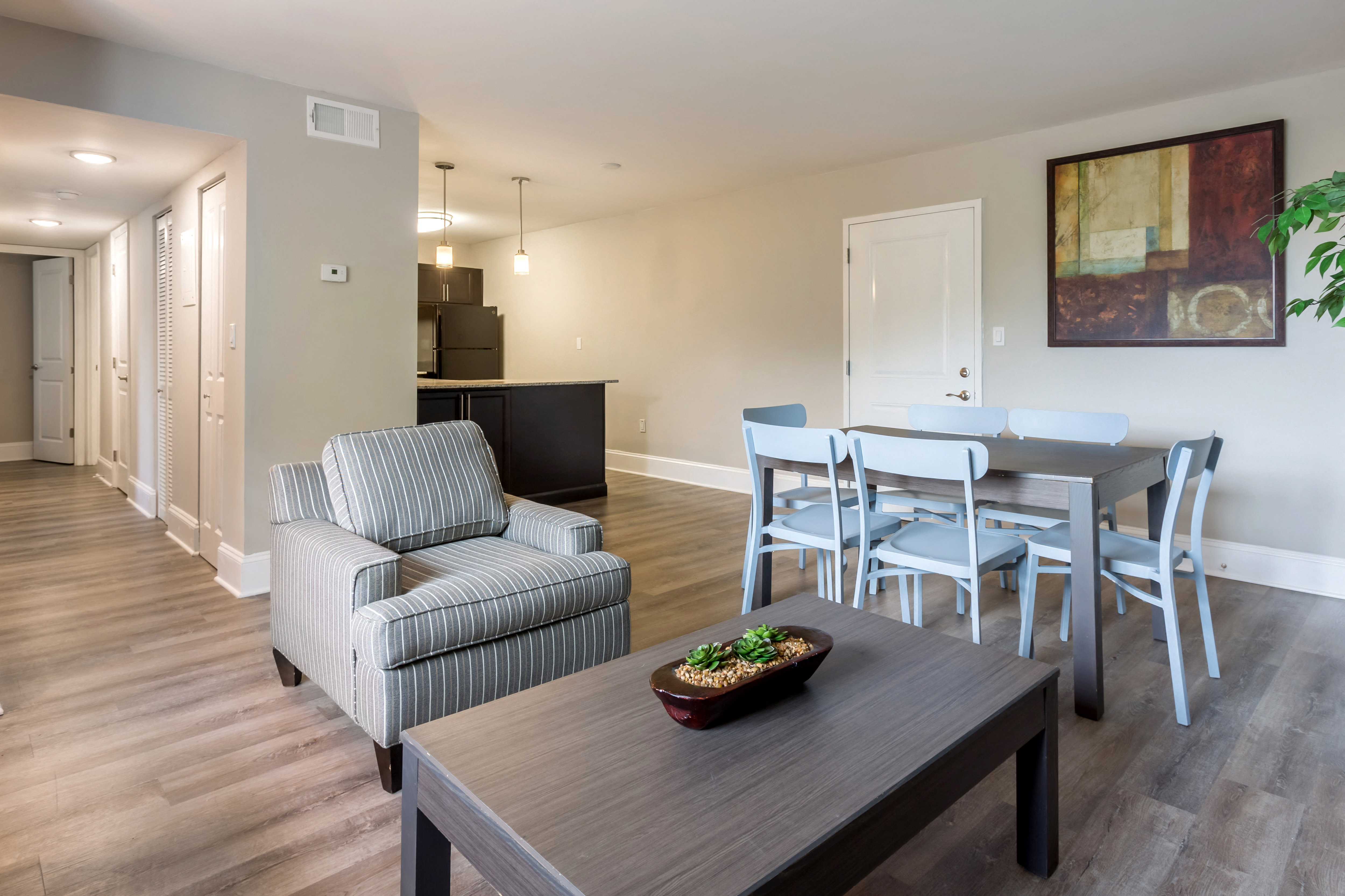 A living room with a grey striped armchair, a wooden coffee table, and a dining table with chairs.