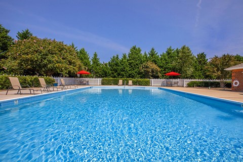Apartment community amenity swimming pool with chairs and umbrellas at  King's Landing Apartments.