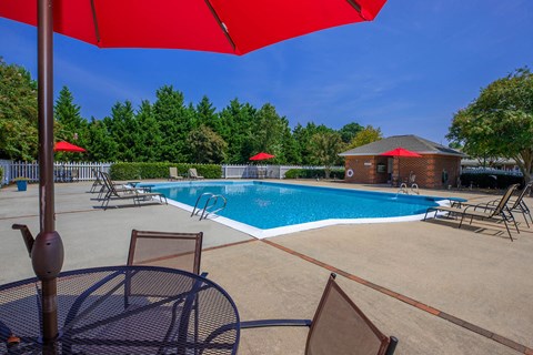 Apartment community amenity swimming pool with chairs and umbrellas at  King's Landing Apartments.