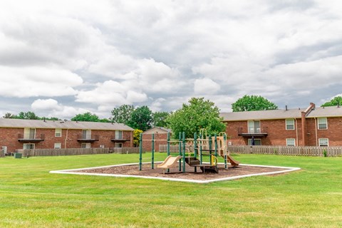 A playground with a slide and swings in the middle of a grassy area.