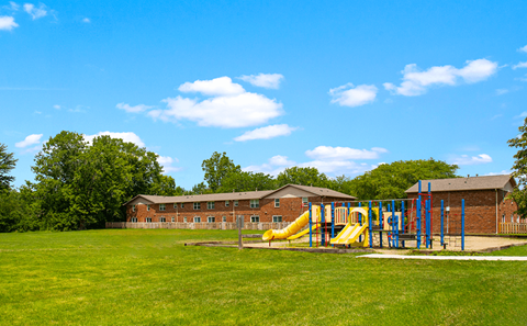 A playground with a yellow slide and a red building in the background.