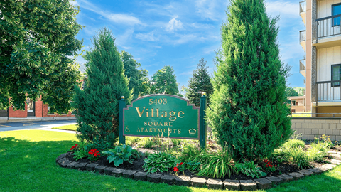 A sign for Village Square Apartments surrounded by greenery.