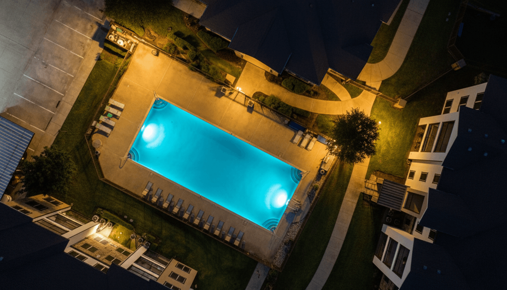 A swimming pool surrounded by lounge chairs and trees at night.