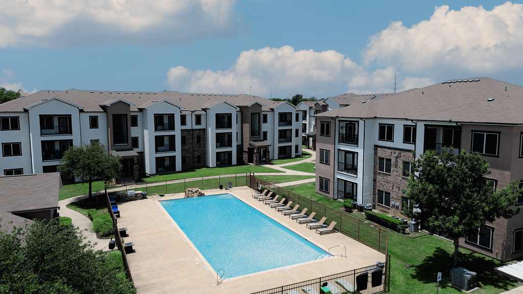 A swimming pool is surrounded by lounge chairs in a residential complex.
