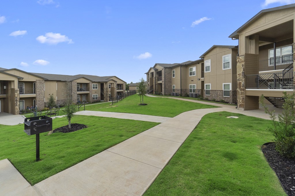 a view of an apartment complex with a green lawn and sidewalk