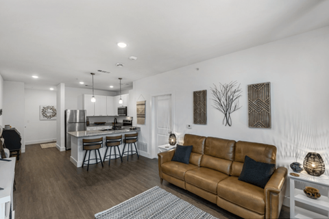 A brown leather couch sits in a living room with a kitchen in the background.