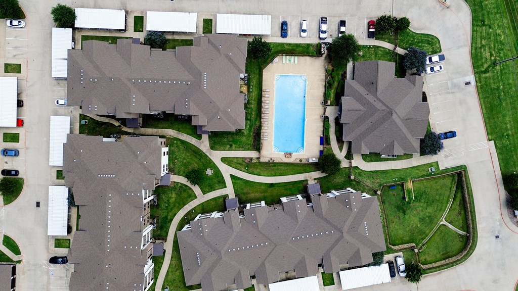 A bird's eye view of a residential area with houses, a swimming pool, and a parking lot.