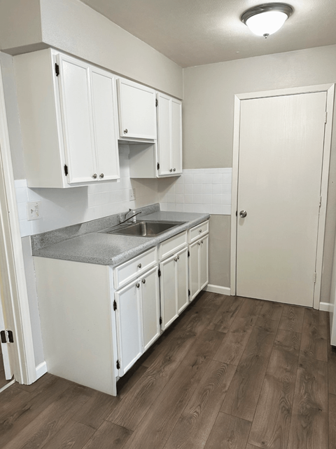 A kitchen with white cabinets and a wooden floor.