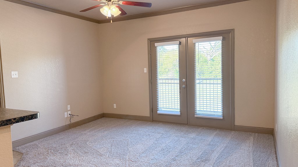 A room with a ceiling fan and sliding glass doors.