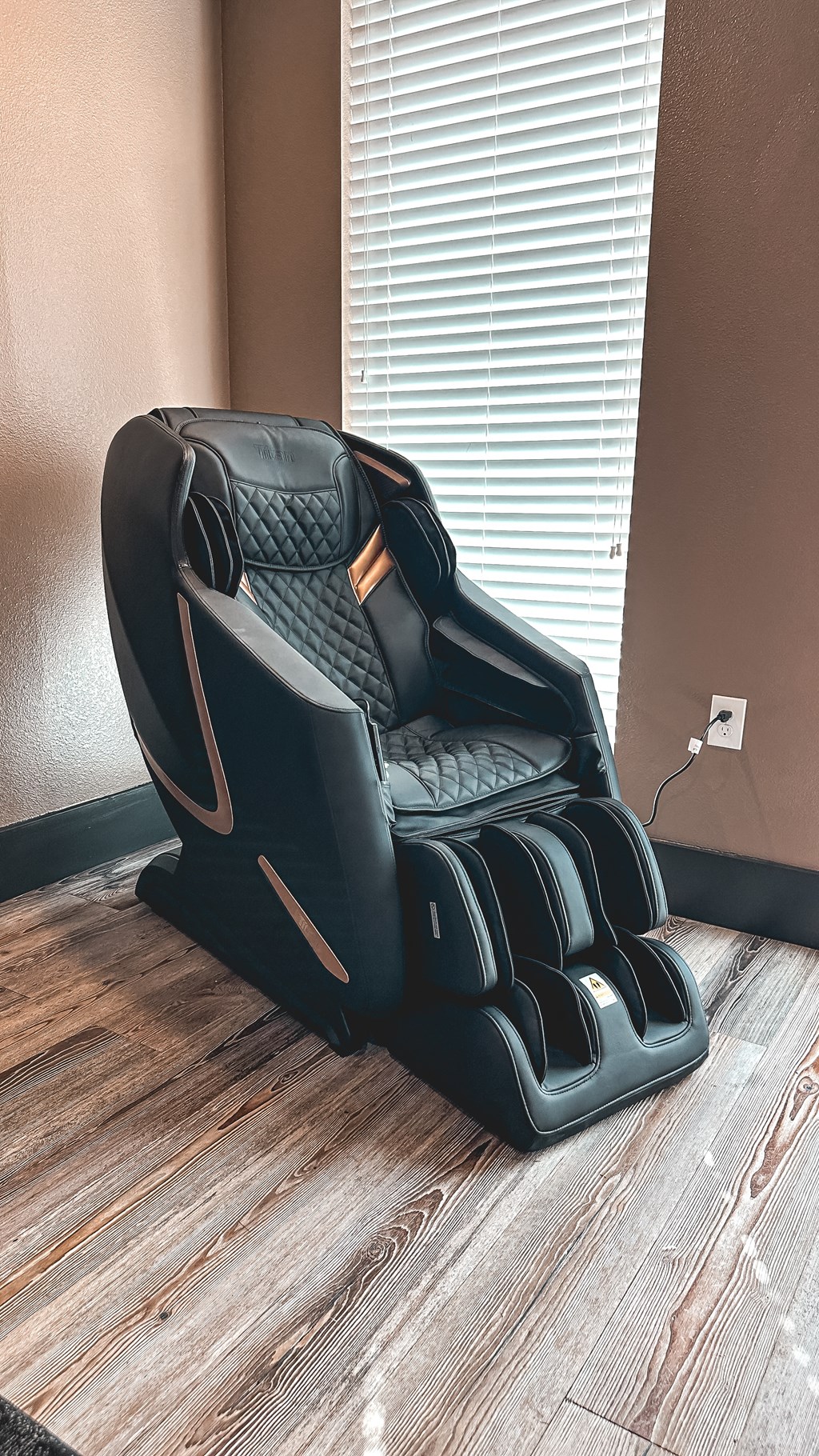 A black massage chair with a wooden base is placed in a room.