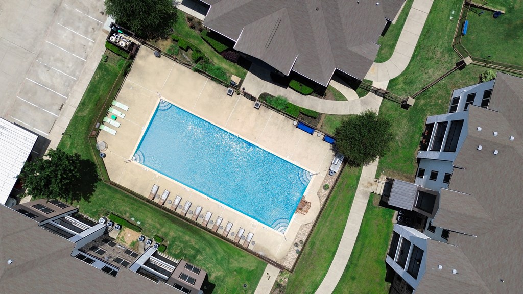 A swimming pool surrounded by a grassy area and apartment buildings.