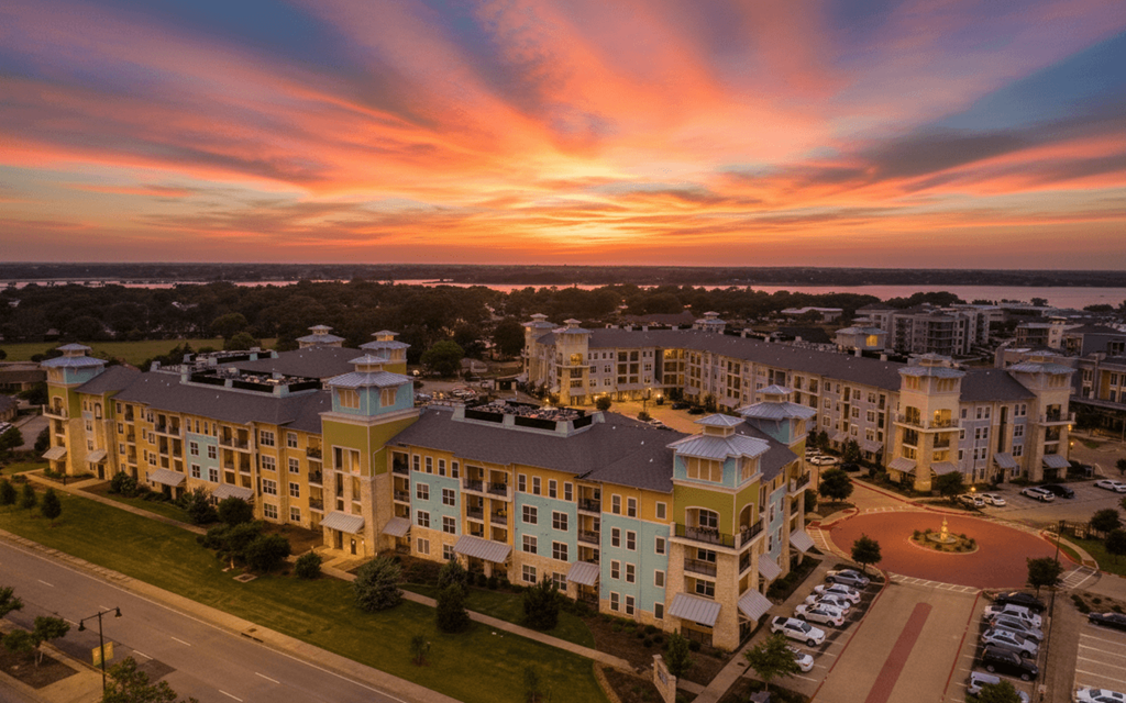 A sunset view of a large apartment complex with a parking lot in front.