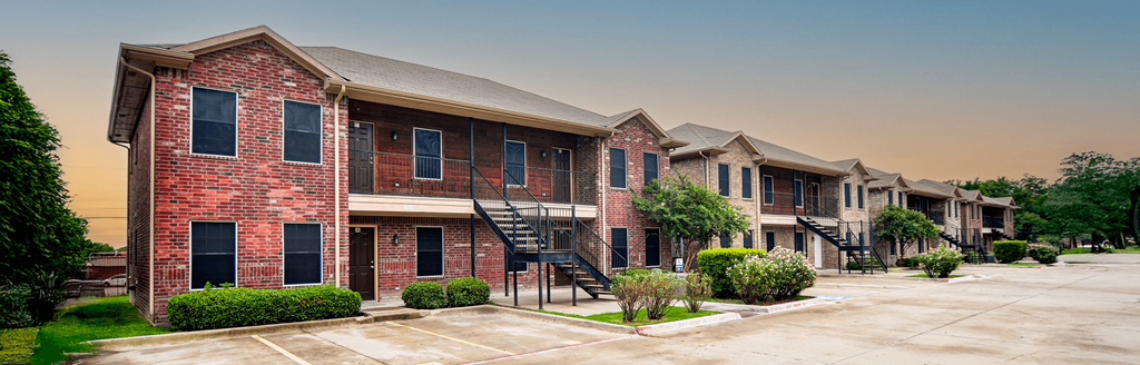 A row of red brick apartment buildings with green bushes in front.