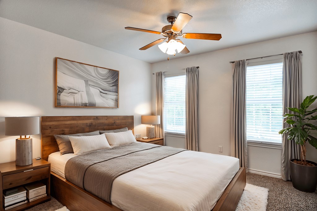 A bedroom with a large bed, a ceiling fan, and a potted plant.