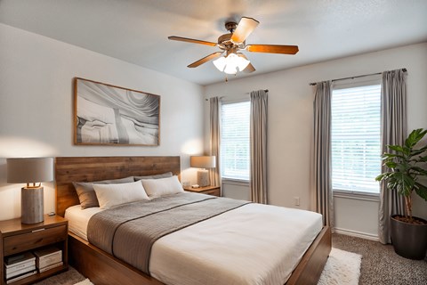 A bedroom with a large bed, a ceiling fan, and a potted plant.