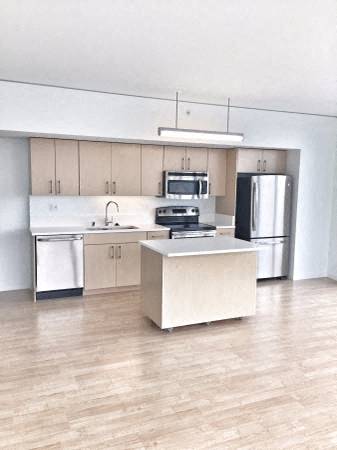 an empty kitchen with stainless steel appliances and a wooden floor