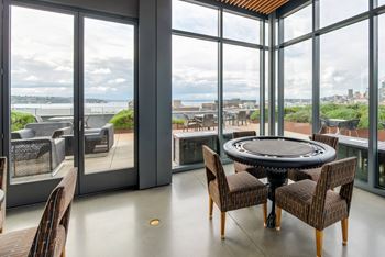 A round table with chairs is set up in a room with a view of the city.