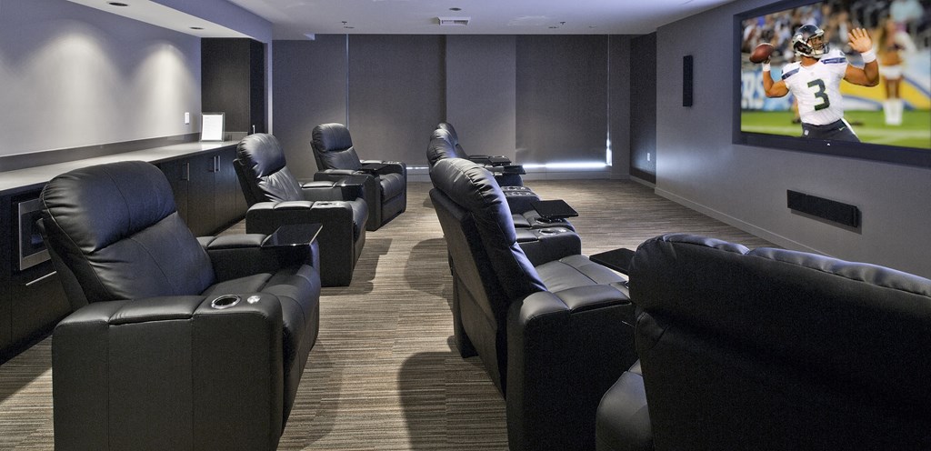 a large screening room with leather chairs and a football game on the tv