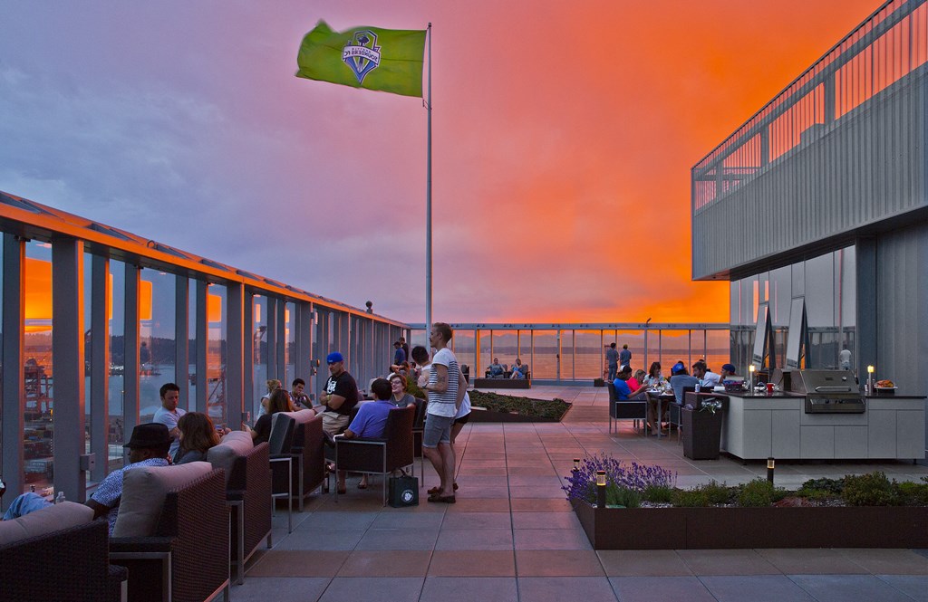 people sitting at tables on a roof terrace at sunset