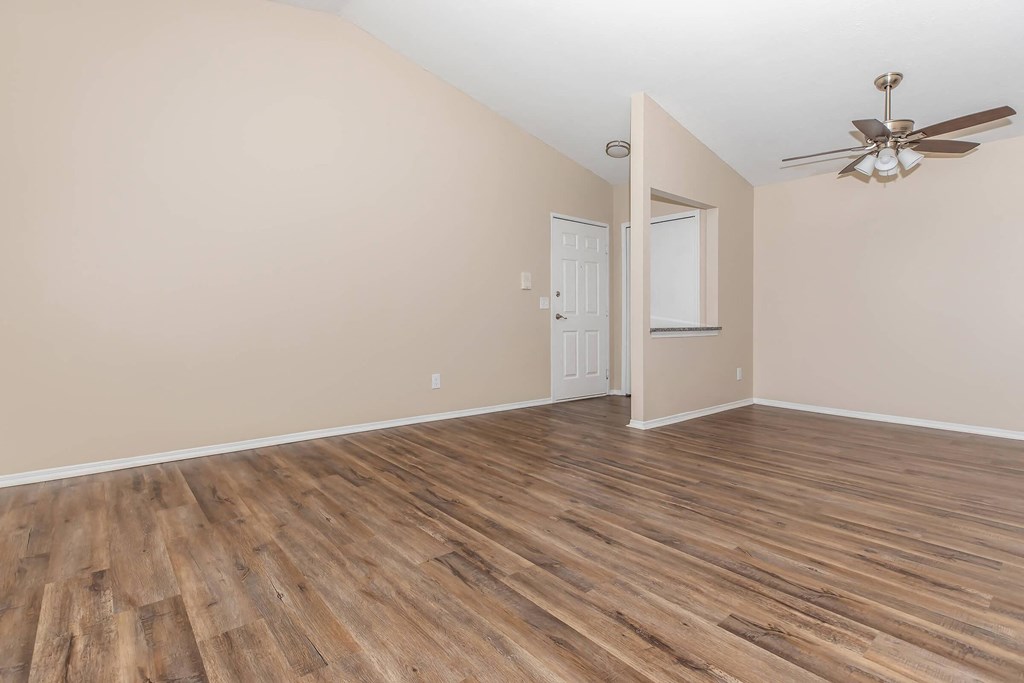 an empty living room with wood floors and a ceiling fan