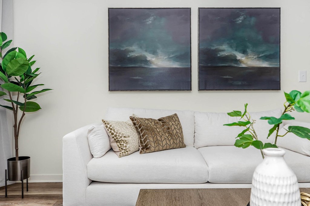 a living room with a white couch and two paintings on the wall