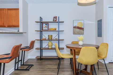 A dining room with a table surrounded by chairs and a shelf with decorative items.