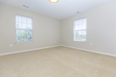 A room with beige carpet and two windows.